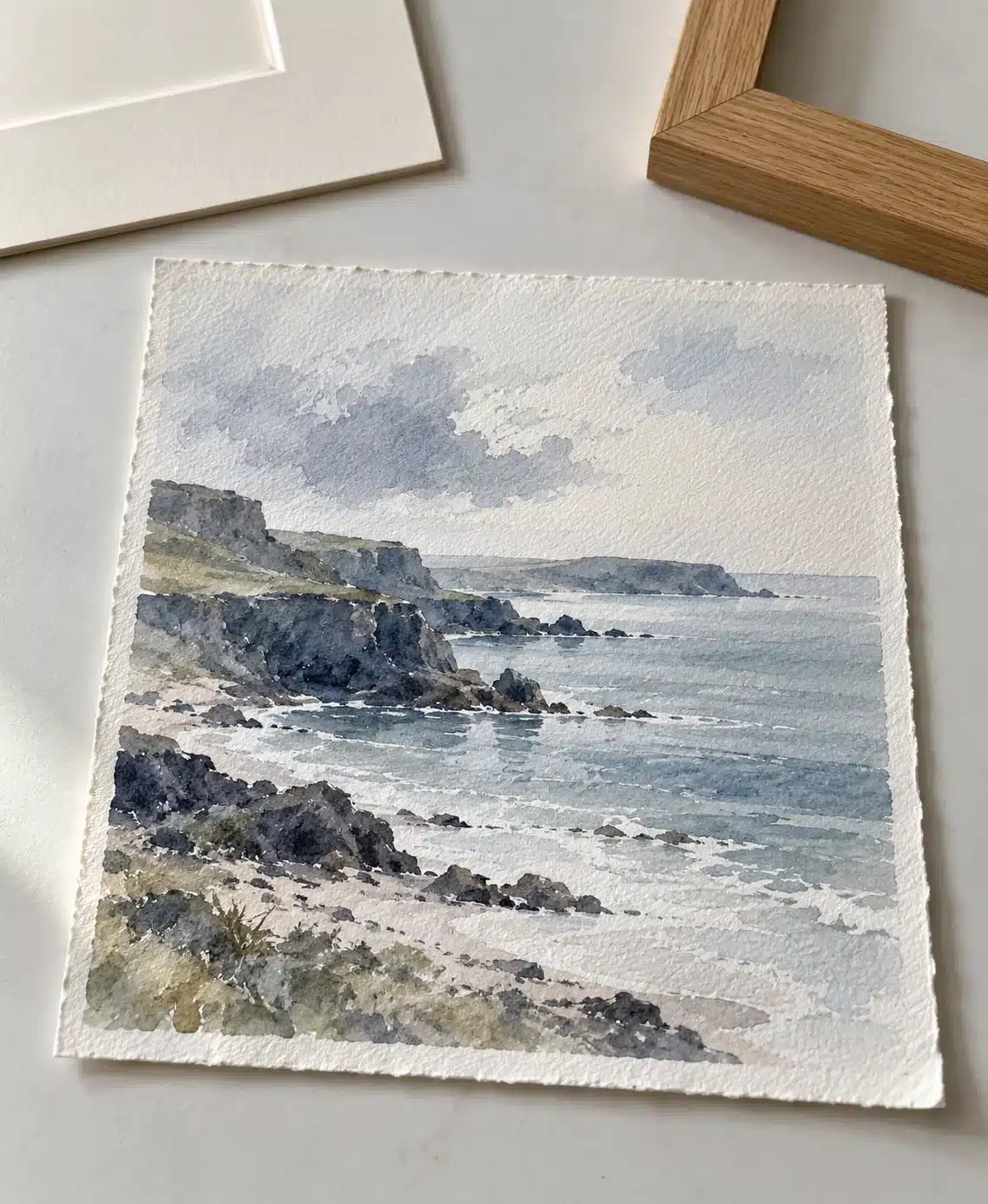 Watercolour paper study with a pale mount and natural oak frame sample on a clean table.